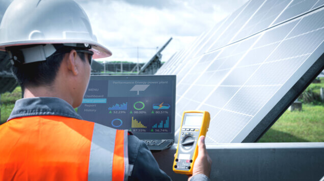 Worker at solar panel in field looking at test instruments